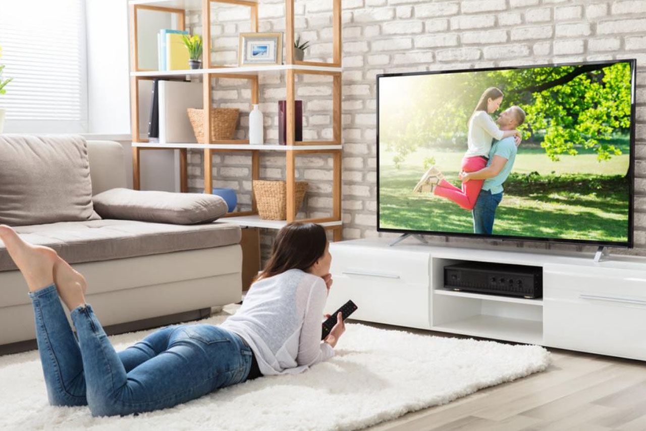 Smart TV postavljen u sobi sa ženskom osobom koja leži na tepihu Smart TV postavljen u sobi sa ženskom osobom koja leži na tepihu